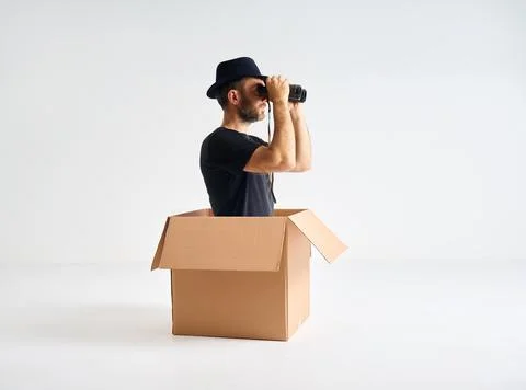 Man in hat looking through binoculars sitting inside cardboard box. Stock-Fotos