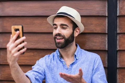 Man with hat making a video call in front of a wooden wall Stock Photos