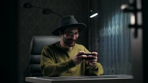 Man in Hat play video game on smartphone sitting at home.Portrait of young guy Stock Footage 232132171