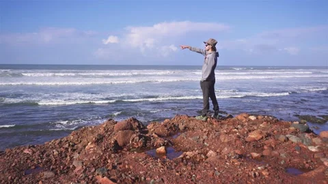 The man in hat points his finger at the open sea in Morocco ocean coast beach Video stock 237940328