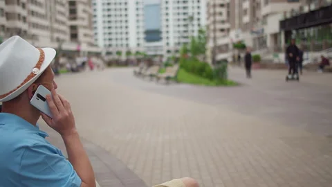 A man in a hat sits on a bench and speaks on the phone, copy space Stock Footage 152734892