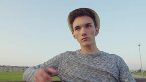 A man in a hat sits on a bench in the open air, corrects his hat, lowers his Stock Footage 315972825