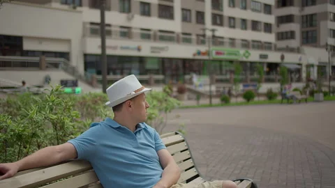 Man in a hat sits on a city bench, resting while walking around the city, camera Stock Footage 155245111