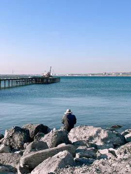 A man in a hat sits on the seashore Stock Photos
