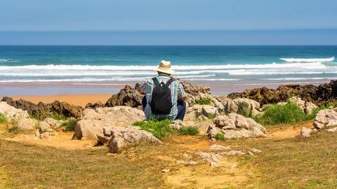 Man with hat sitting with his back to him and enjoying the sea views in northern Stock Photos