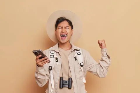 A man in a hat smiles while holding a cell phone and binoculars Foto stock