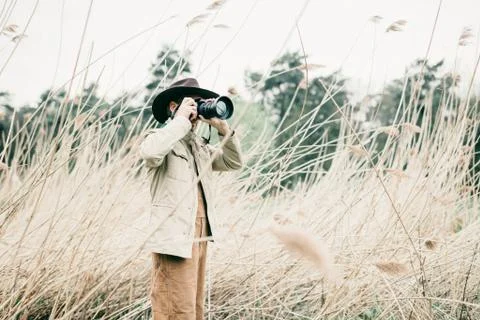 Man with hat standing between reed photographing nature. Stock Photos