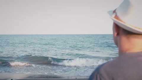 Man in hat standing on the seashore watching the waves, back view Stock Footage 304846290