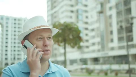 Man in a hat talking on a mobile phone while standing , background of buildings Stock Footage 152913893