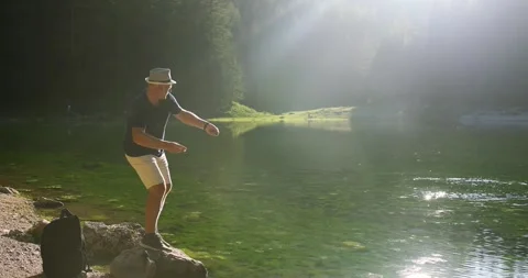 A man in a hat throws pebbles on the surface of the water on the lake Stock Footage 247662935