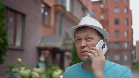 Man in hat walking around the city talking on a mobile phone, camera tracking 스톡 동영상 137459374