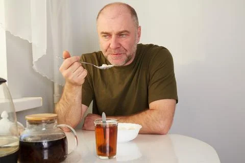 A man is having breakfast at the kitchen table, eating porridge from a bowl.. 写真素材