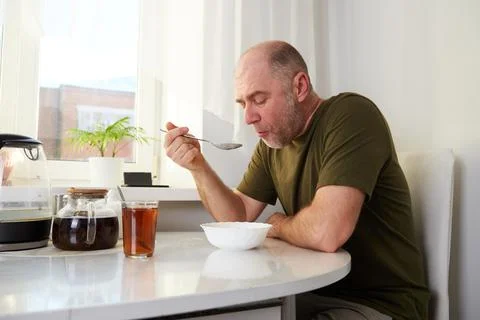 A man is having breakfast at the kitchen table, eating porridge from a bowl.. Stock Photos