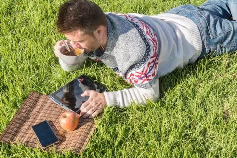Man having breakfast lying on the grass in the garden with technology Stock Photos