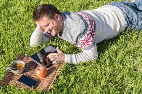 Man having breakfast lying on the grass in the garden with technology Stock Photos
