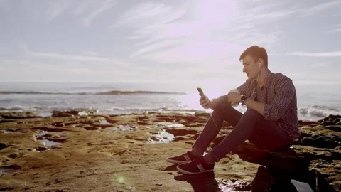 Man is having a conversation over his smartphone while sitting on a coast Stock Footage 75742251