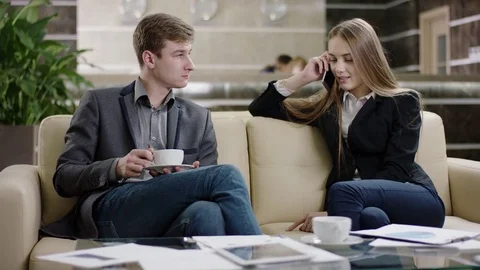 Man having a cup of coffee and girl talking on phone in lobby Stock Footage