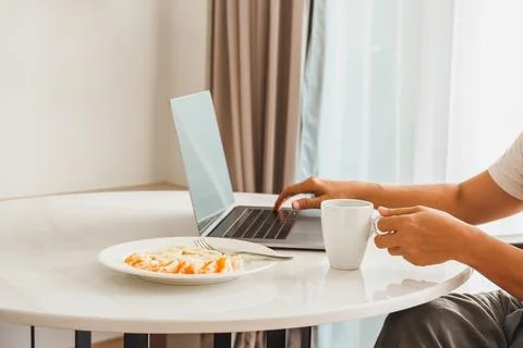 Man having cup of coffee with fresh fruits while working on laptop. Stock Photos