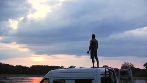 Man having a drink on top of his caravan at sunset Video stock 135381508