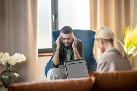 Man having headache while talking to psychologist Stock Photos