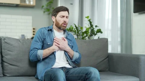 Man having heart attack sitting alone at home on the sofa. Mature bearded Stock Footage 231232736