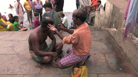 A man having his head shaved by a hairdresser on the ghats, steps by the Ganges. Stock-Footage 63210913