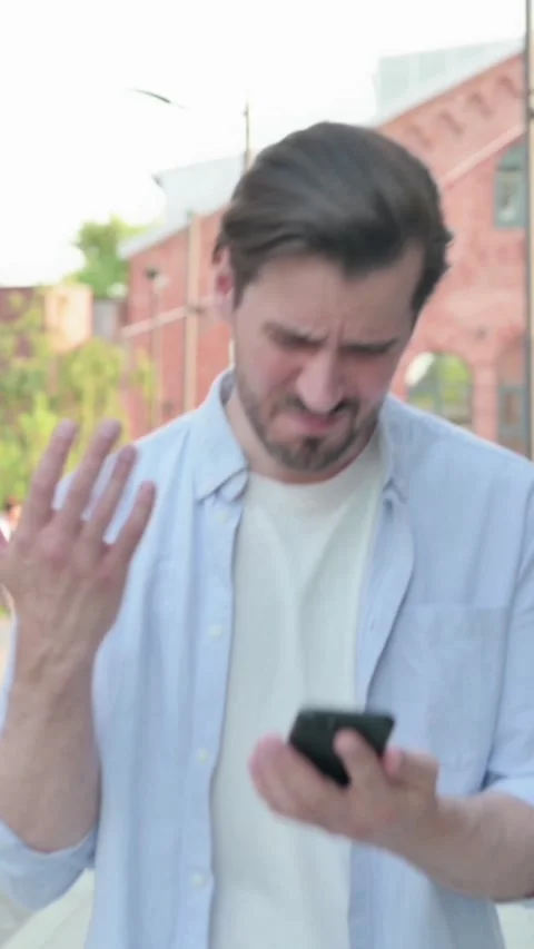 Man Having Loss on Phone while Walking in Street, Vertical Video Stock Footage 339666437