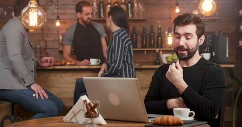 A man having an online call at his laptop while working in a coffee shop. Stockbeeldmateriaal 103370385