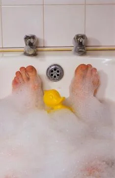 Man having soak in bubble bath with plastic toy duck Stock Photos
