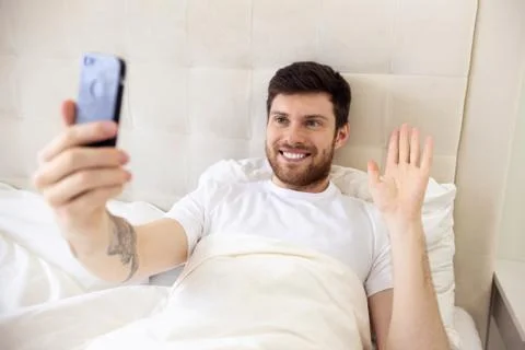 Man Having Video Call in Bed on Phone. Home Video Call. Work at Home From Bed Stock Photos