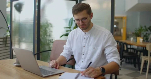 Man having video call on laptop and making notes in notebook while sitting in Stock Footage 160770912