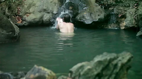Man is having a wash in a small waterfall on the river Stock Footage 49389884