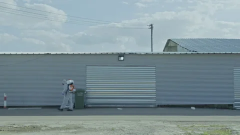 Man in a hazmat suit spraying outside an industrial building Stock Footage 275190828