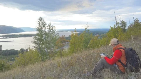 Man He is sitting in the mountains,  using tablet and looking through binoculars Stock Footage 70013989