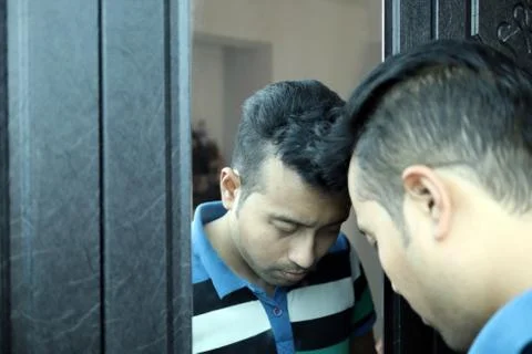 A man with head down in front of a mirror in depressed mood with selective focus Stock Photos