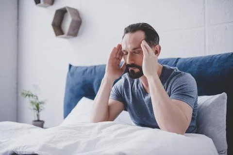 Man with headache sitting on bed Stock Photos