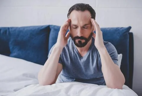 Man with headache sitting on bed Stock Photos