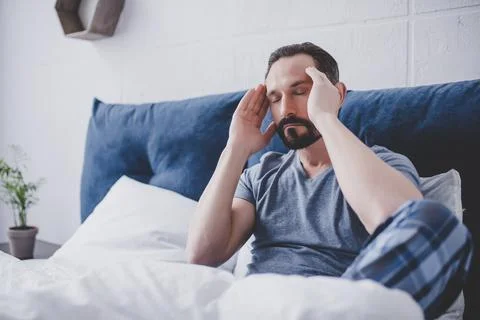 Man with headache sitting on bed Stock Photos