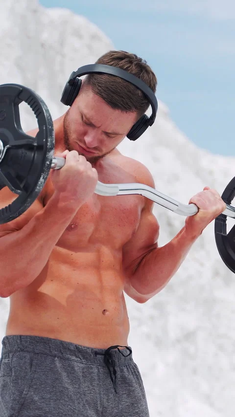 A man in headphones does barbell biceps exercises. Workout in nature Stock Footage 274409671