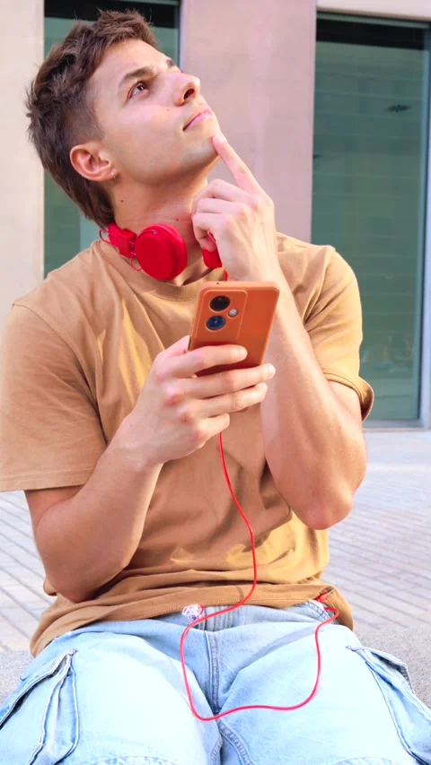 Man with headphones looking up while holding smartphone in urban city.Vertical Stock Footage 293568974