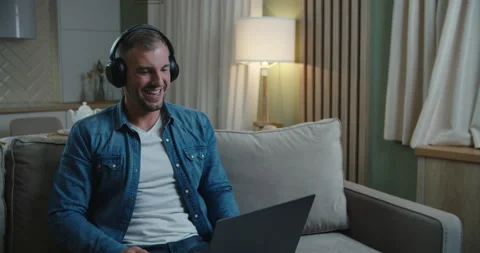 Man headphones sit at sofa in front of pc talking with business partner by video Stock Footage 146769343