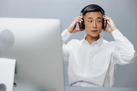 Man in headphones at the table in front of the computer Gray background Stock Photos