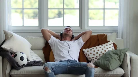 A man in Headphones Using Smartphone Sitting On sofa Indoor. Stock Footage 163087722
