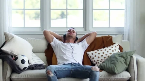 A man in Headphones Using Smartphone Sitting On sofa Indoor. Stock Footage 163087737