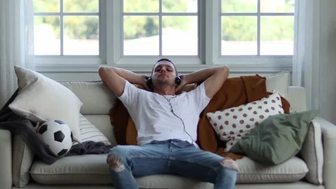 A man in Headphones Using Smartphone Sitting On sofa Indoor. Stock Footage 163087780