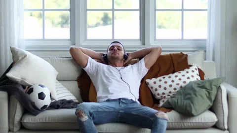 A man in Headphones Using Smartphone Sitting On sofa Indoor. Stock Footage 163087808