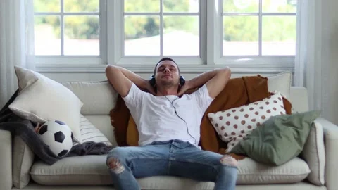 A man in Headphones Using Smartphone Sitting On sofa Indoor. Stock Footage 163087834