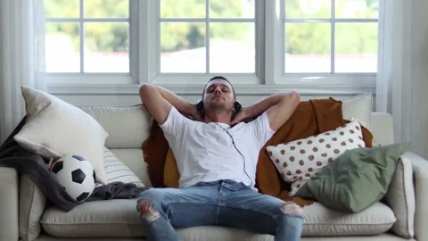 A man in Headphones Using Smartphone Sitting On sofa Indoor. Stock Footage 163087843