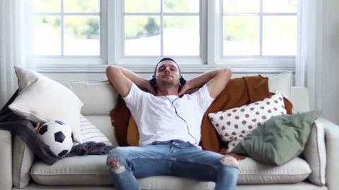 A man in Headphones Using Smartphone Sitting On sofa Indoor. Stock Footage 163087850