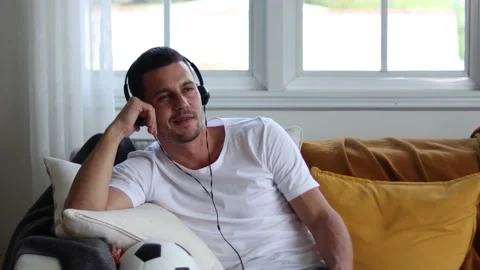 A man in Headphones Using Smartphone Sitting On sofa Indoor. Stock Footage 163087997